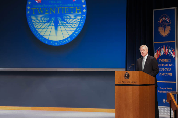 US-Außenminister Mike Pompeo trägt einen schwarzen Blazer, ein weißes Hemd und eine schwarze Krawatte und steht vor einem blauen Hintergrund an einem Podium mit zwei Mikrofonen, während er auf der 20. Internationalen Seemacht-Symposium spricht, rechts neben ihm eine Reling.