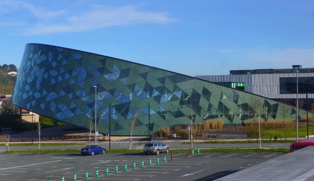 Der neue Sitz des Europäischen Parlaments in Brüssel, Belgien, ein großes Gebäude mit zahlreichen Autos davor, umgeben von Straßenlaternen, Straßenschildern, Büschen, Bäumen und einem bewölkten Himmel.