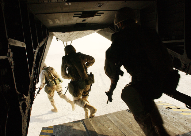 Soldaten in Uniform und Helmen steigen aus einem Flugzeug aus und halten dabei Gewehre während einer Mission.