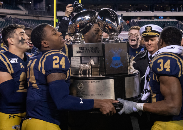 Eine Gruppe von Männern, die einen Pokal vor einem jubelnden Publikum in einem hell erleuchteten Stadion halten, wobei der Mann in der Mitte eine Kamera hält.