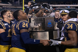 Eine Gruppe von Männern, die einen Pokal vor einem jubelnden Publikum in einem hell erleuchteten Stadion halten, wobei der Mann in der Mitte eine Kamera hält.