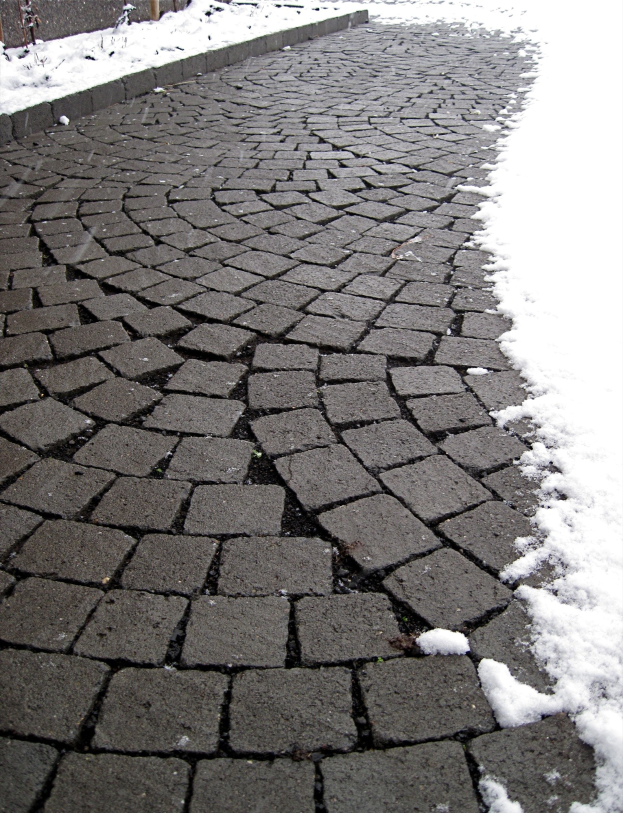 Eine Kopfsteinpflasterstraße mit leichtem Schnee auf dem Boden, gesäumt von einem Zaun im Hintergrund, der eine ruhige Winterszene zeigt.