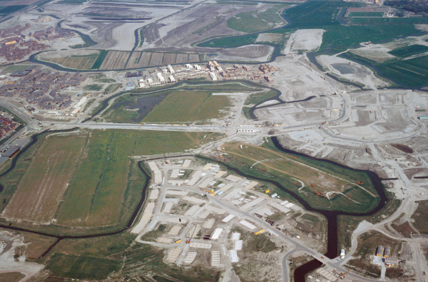 Eine Luftaufnahme einer Stadt mit Gebäuden, Straßen, Feldern und Bäumen, die einen großen Wasserbereich in der Mitte zeigt, der wahrscheinlich ein Deponie ist.