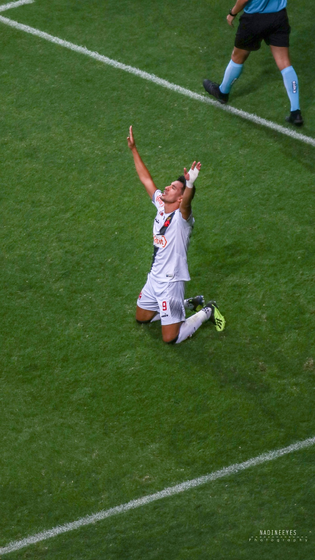 Ein Fußballspieler in Uniform kniet auf dem Feld und streckt die Arme aus, um zu feiern.