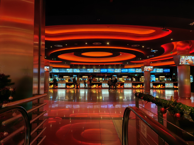 Ein Casino-Innenraum mit einem Weihnachtsbaum in der Mitte, gefliesten Böden, Geländern auf beiden Seiten, geschmückten Säulen und Deckenleuchten, mit Menschen im Hintergrund, die eine festliche Atmosphäre schaffen.