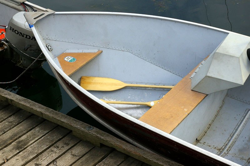 Kleines Boot mit zwei Paddeln und einem Motor auf einem hölzernen Steg, der auf dem Wasser schwimmt.