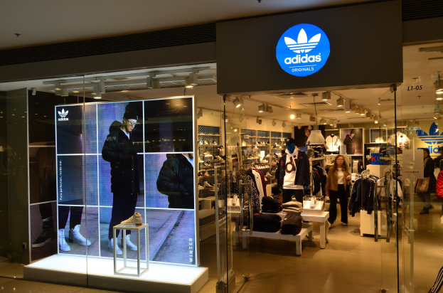 Verkaufsfläche eines adidas Originals-Geschäfts in einem Einkaufszentrum mit Schaufensterpuppen, Kleiderständern, Schuhständern und beleuchteter Markenwerbung.