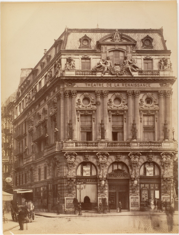 Schwarz-weiß-Fotografie des Théâtre de la Renaissance in Paris mit seiner prächtigen Fassade, die Fenster, Säulen, Bögen und Skulpturen aufweist, mit ein paar Menschen und Fahrzeugen auf der Straße davor und dem Himmel im Hintergrund.