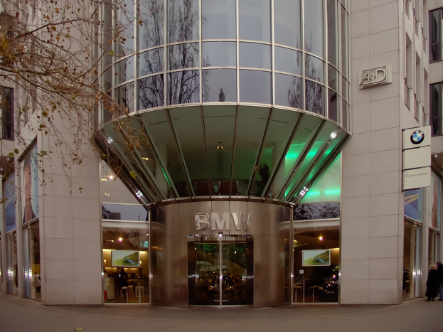 Moderner BMW-Hauptsitz in Frankfurt mit Glasfassaden und Text auf der Fassade, Menschen vor dem Gebäude und einem Baum links.
