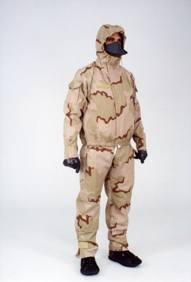 Eine Person in einem Tarnmuster-Schutzoverall mit Kapuze und Maske steht vor einem weißen Hintergrund.