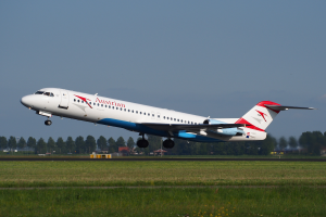Ein Embraer ERJ-190-Flugzeug der Austrian Airlines beim Abheben vom Frankfurter Flughafen, mit grünem Gras, Bäumen und Gebäuden im Hintergrund und dem Himmel darüber.