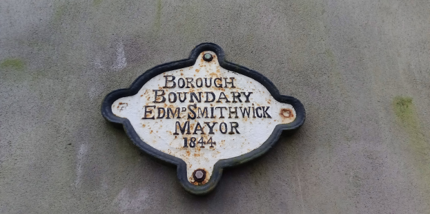 Metallplakette an einer Gebäudeseite mit schwarzem Hintergrund und weißer fettgeschriebener Schrift, die "Stadtgrenze Edm Smithwick Bürgermeister" liest.