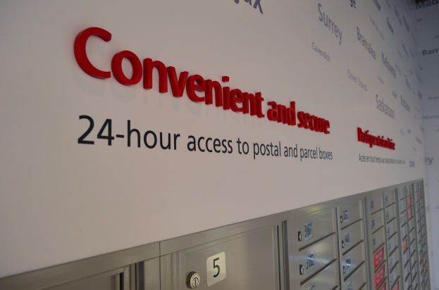 Wandtafelwerbung für 24-Stunden-Zugang zu Post- und Paketfächern, mit nummerierten Fächern darunter.