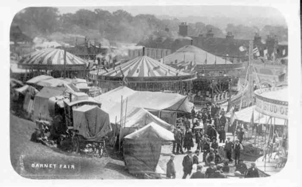 Schwarzes und weißes Foto eines Karnevals mit Zelten, Menschen, Karren, Pfählen, Bäumen und Gebäuden, beschriftet mit "Barnet Fair, London, England."