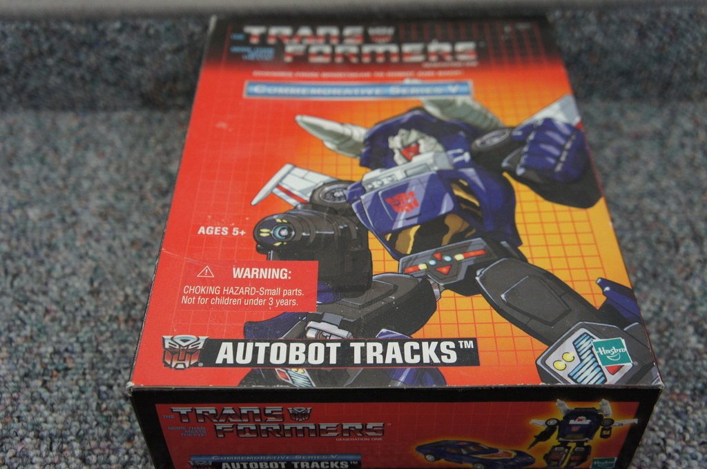 Roter, oranger und blauer AUTOBOT TRACKS-Roboterkasten mit weißer Schrift auf einem unscharfen schwarzen Hintergrund.