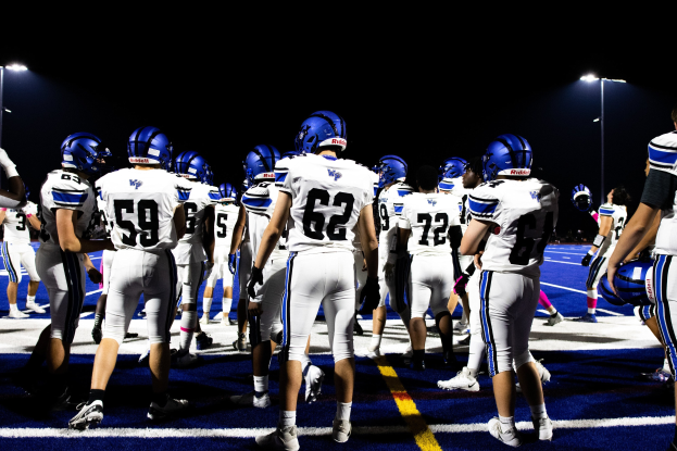 Gruppe von Fußballspielern in Helmen und Stollenschuhen auf einem Feld unter Flutlichtmasten, bereit für ein Spiel.