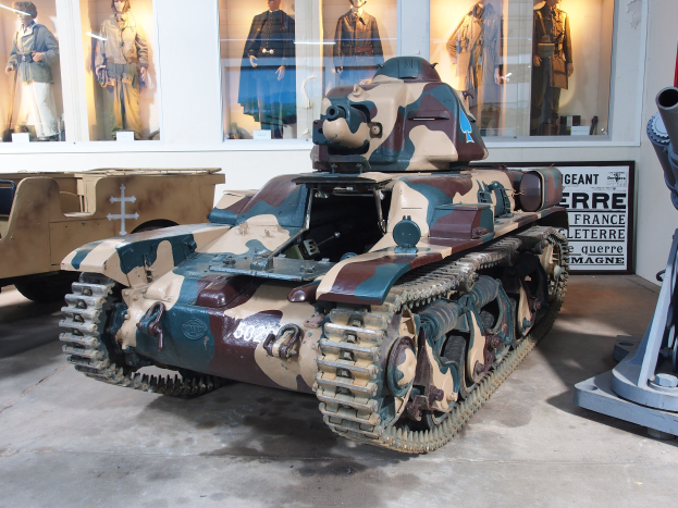 Alter Panzer aus dem Zweiten Weltkrieg in einem Museum ausgestellt, umgeben von anderen Militärfahrzeugen, mit einer Maschine rechts und Uniformen tragenden Schaufensterpuppen im Hintergrund.