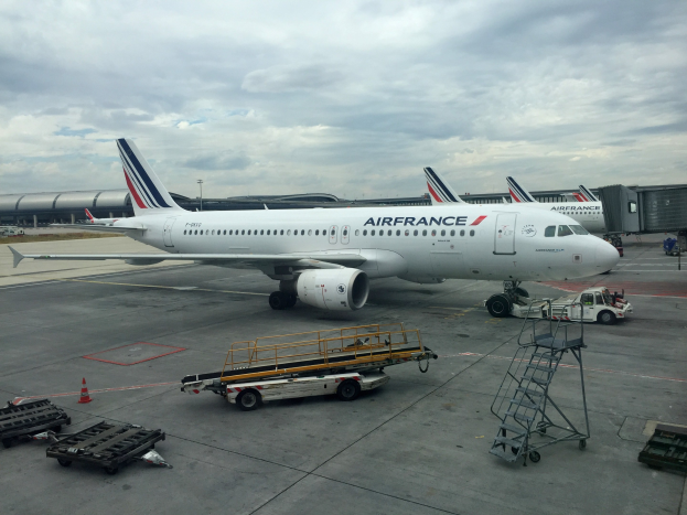 Air France Airbus A320-200 auf dem Rollfeld am Pariser Charles-de-Gaulle-Flughafen mit Bodenfahrzeugen, Verkehrskegeln und Equipment im Hintergrund.