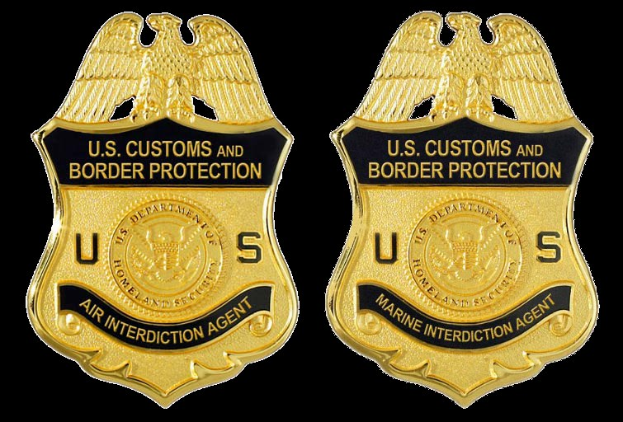 Zwei goldfarbene Abzeichen mit 'U.S. Customs and Border Protection'-Text vor einem weißen Hintergrund.