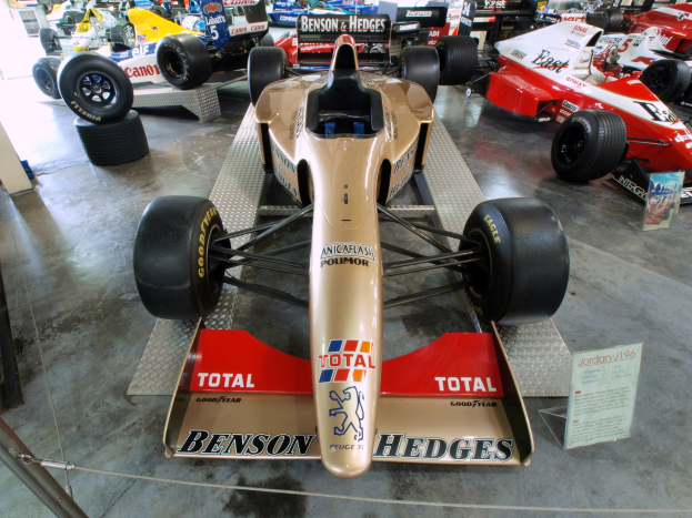 Rennwagen in einem Motorsportmuseum ausgestellt, durch einen Metallzaun von Besuchern und Informationsschildern getrennt.