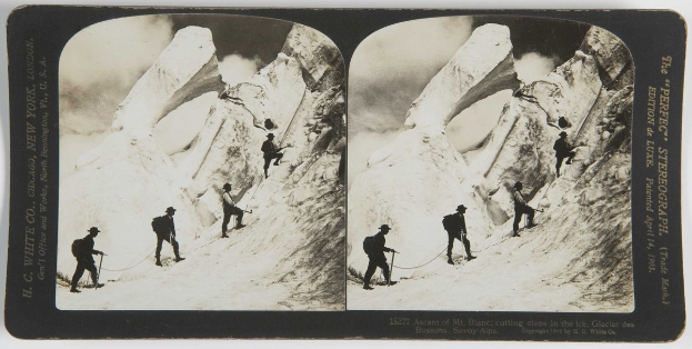 Schwarzes und weißes Foto einer Gruppe von Menschen, die einen schneebedeckten Berg mit den Eisschritten des Mt. Blanc im Hintergrund erklimmen, mit Rückenpacken und Seilen.