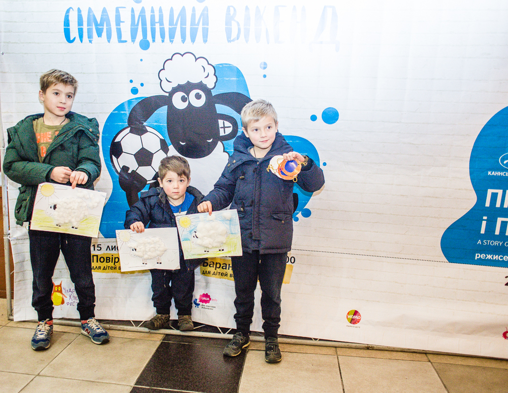 Drei Kinder stehen mit Papieren vor einem Banner.